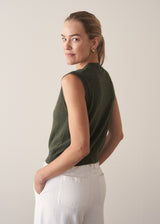 Woman wearing dark green fine knit sweater with removable heart brooch with white barrel leg jeans