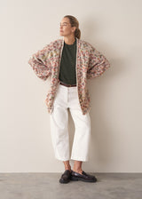 Woman wearing dark green fine knit sweater with removable heart brooch with white barrel leg jeans