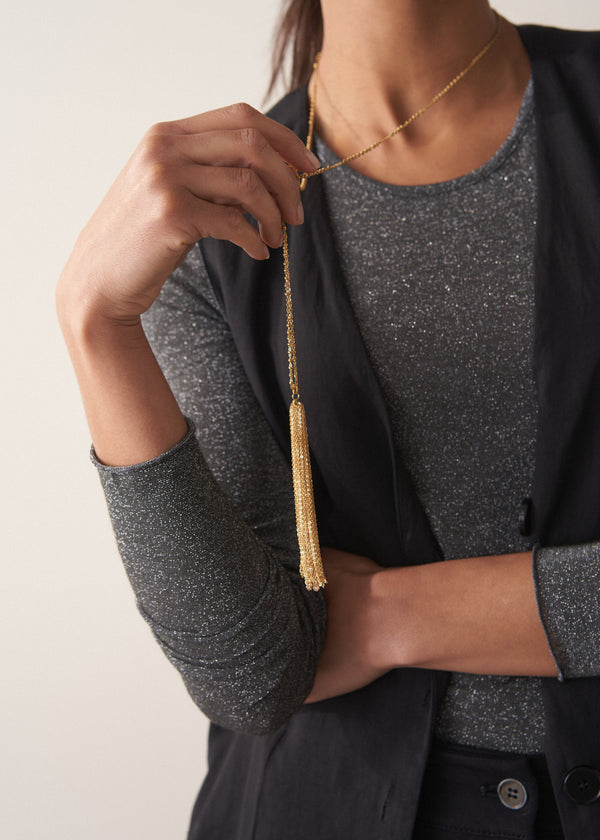 Model wearing a long chain necklace with gold beads, finished with a multi-strand pendant, and colourful crystals