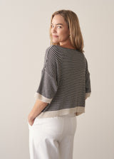 Woman wearing navy and white stripe light knitted sweater and white barrel leg jeans