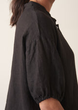 Woman wearing a black linen top and striped, cropped satin trousers against plain background