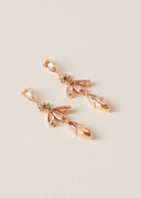 A pair of drop earrings with cascading peach crystals in a floral design, on a beige background