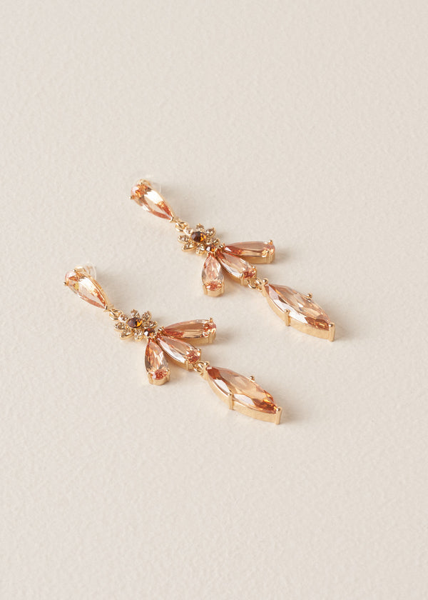 A pair of drop earrings with cascading peach crystals in a floral design, on a beige background