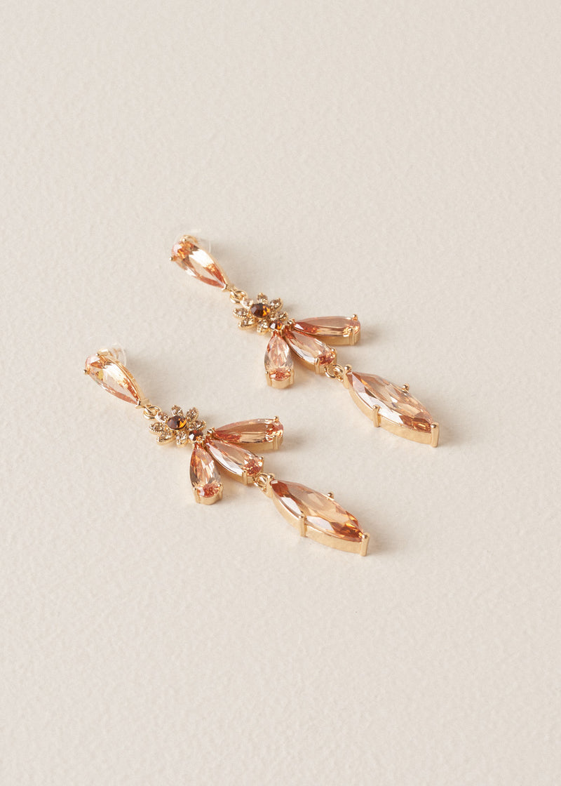 A pair of drop earrings with cascading peach crystals in a floral design, on a beige background
