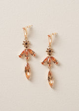A pair of drop earrings with cascading peach crystals in a floral design, on a beige background