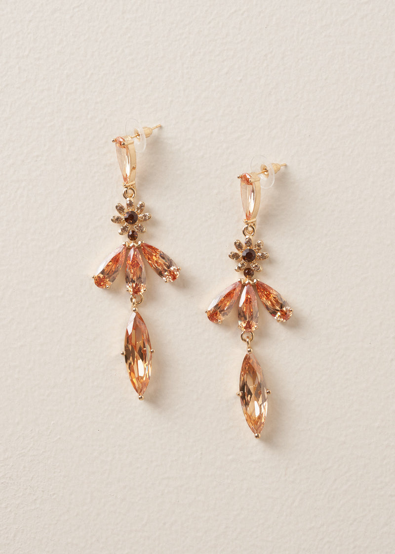 A pair of drop earrings with cascading peach crystals in a floral design, on a beige background