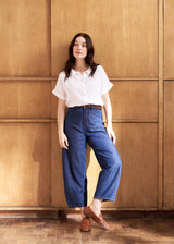 Model wearing a white linen short sleeve shirt with blue jeans and loafers, against a wooden background