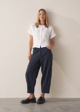 Woman wearing short sleeve white boxy linen shirt and dark navy trousers with black loafers