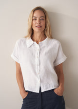 Woman wearing a button down short sleeve white boxy linen shirt and dark navy trousers