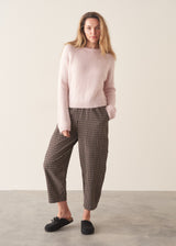 A woman wearing a pale pink boxy sweater with dark check barrel leg trousers