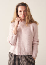 A woman wearing a pale pink boxy sweater with dark check barrel leg trousers