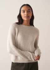 Woman wearing a round neck pale knit sweater against a plain background