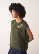 Person wearing a green knitted sleeveless sweater with a silver beaded embellishment 
