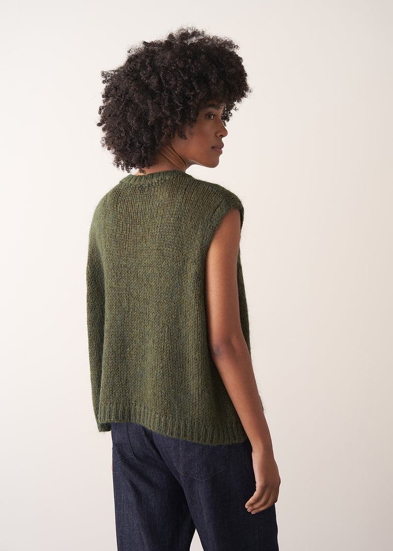 Person wearing a green knitted sleeveless sweater with a silver beaded embellishment 