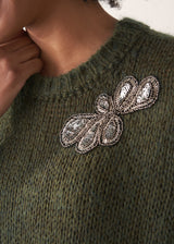 Person wearing a green knitted sleeveless sweater with a silver beaded embellishment 