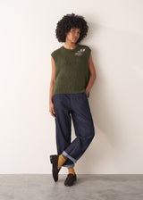 Person wearing a green knitted sleeveless sweater with a silver beaded embellishment 