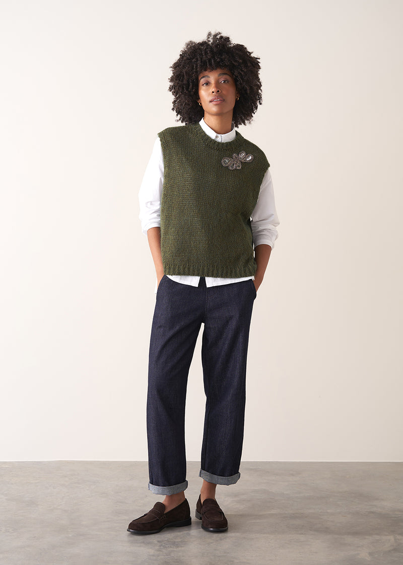 Person wearing a green knitted sleeveless sweater with a silver beaded embellishment 