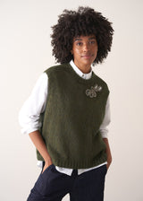 Person wearing a green knitted sleeveless sweater with a silver beaded embellishment 