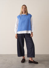 Woman wearing blue knitted sleeveless sweater, a white shirt and dark blue jeans