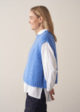 Woman wearing blue knitted sleeveless sweater, a white shirt and dark blue jeans