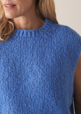 Woman wearing blue knitted sleeveless tank and dark blue jeans