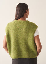 A woman wearing a bright green sleeveless sweater with a white t-shirt and charcoal checked barrel leg trousers