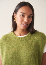 A woman wearing a bright green sleeveless sweater with a white t-shirt and charcoal checked barrel leg trousers