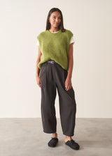 A woman wearing a bright green sleeveless sweater with a white t-shirt and charcoal checked barrel leg trousers