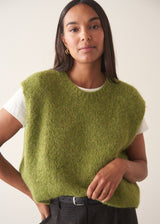 A woman wearing a bright green sleeveless sweater with a white t-shirt and charcoal checked barrel leg trousers
