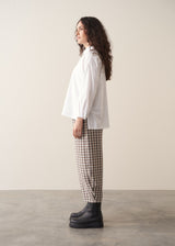 Model wearing neutral check barrel leg trousers and a white shirt