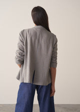 A woman models a blue-green checked cotton jacket over a white shirt, paired with blue jeans, set against a beige background