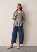 A woman models a blue-green checked cotton jacket over a white shirt, paired with blue jeans and white loafters, set against a beige background