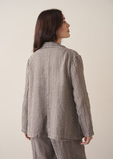 A woman models a grey and black checked linen jacket with matching barrel leg linen checked trousers, set against a beige background