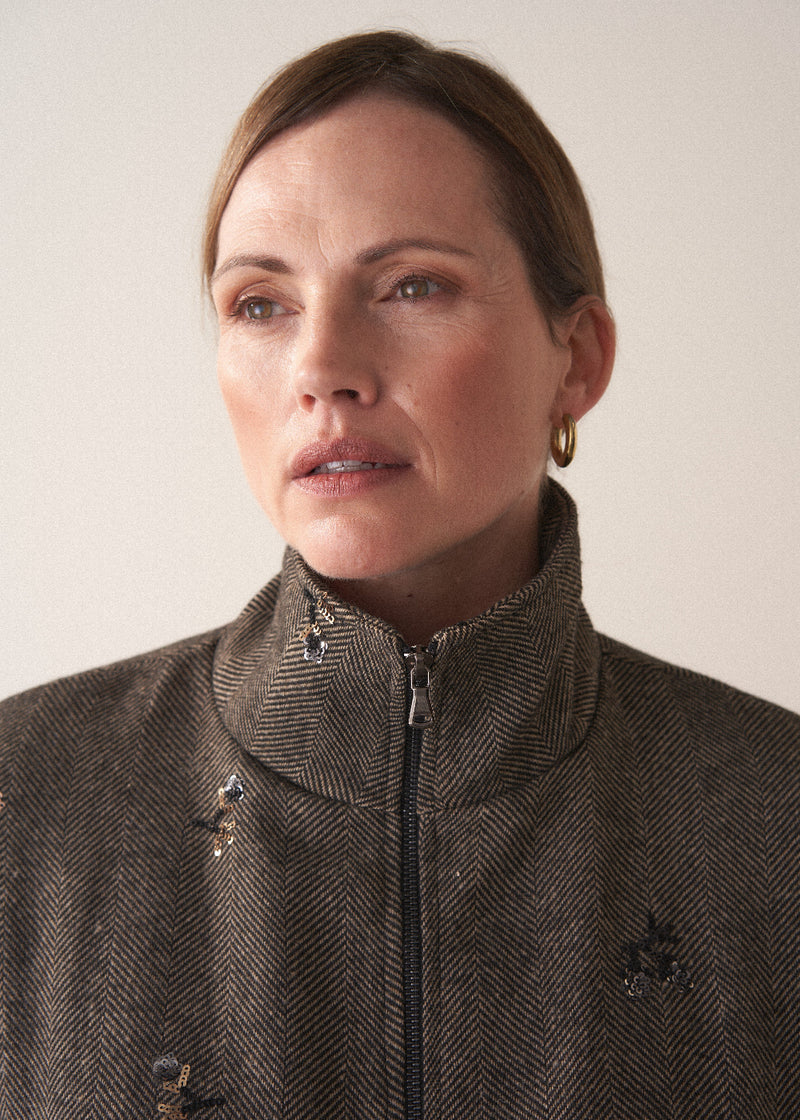 Close up of zip detail of woman wearing brown herringbone bomber jacket with sequin embelishment