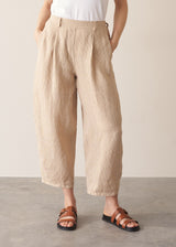 Woman wearing a white vest top and beige striped ankle length barrel leg linen trousers 
