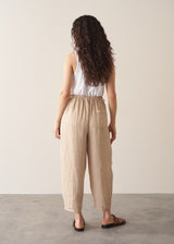 Woman wearing a white vest top and beige striped ankle length barrel leg  linen trousers 