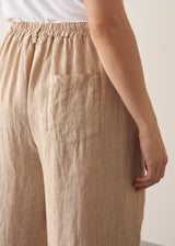 Woman wearing a white vest top and beige striped ankle length barrel leg  linen trousers 