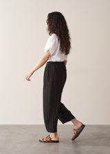 Woman wearing white linen shirt and black ankle length linen barrel leg trousers