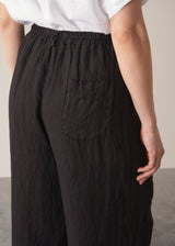 Woman wearing white linen shirt and black ankle length linen barrel leg trousers