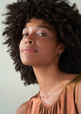 Woman wearing contemporary gold hoop earrings with crystal detail, styled  with a satin top