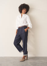A woman wearing a white, embroidered detail shirt with blue denim jeans.