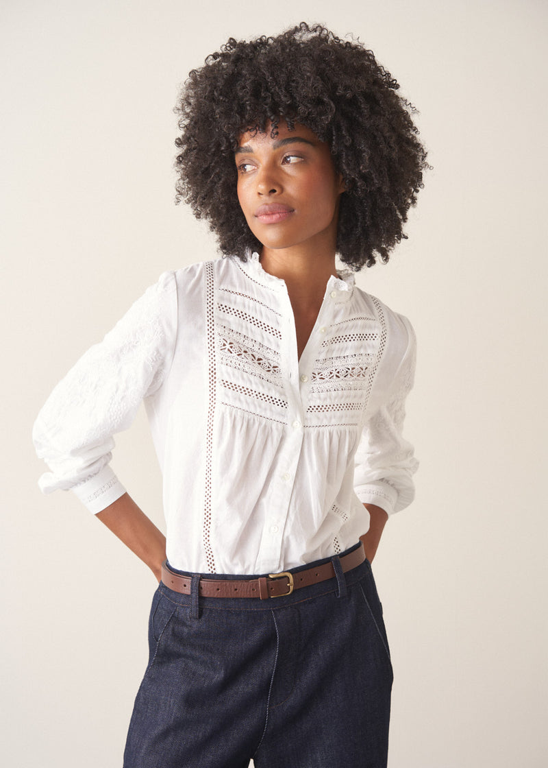A woman wearing a white, embroidered detail shirt with blue denim jeans.