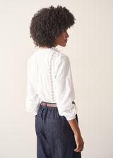 A woman wearing a white, embroidered detail shirt with blue denim jeans.