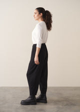 A woman wearing a white top and black barrel leg trousers with chunky boots against a plain background