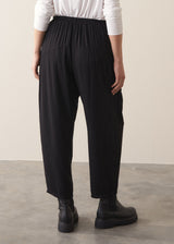 A woman wearing a white top and black barrel leg trousers and chunky boots against a plain background