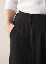 A woman wearing a white top and black barrel leg trousers against a plain background