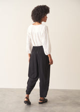 A woman wearing a white v-neck top and black slimtapered trousers.