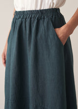 Woman wearing dark green linen cocoon skirt with grey jumper