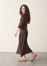 Woman wearing a brown patterned dress walking on a plain background