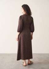 Woman wearing a brown patterned dress standing against a plain background